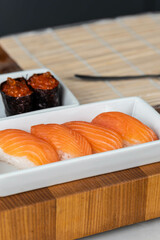 Close up of sushi chef hands preparing japanese food. Man cooking sushi with red caviar and salmon at restaurant. Traditional asian seafood rolls on cutting board.
