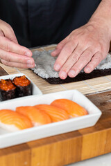 Close up of sushi chef hands preparing japanese food. Man cooking sushi with red caviar and salmon at restaurant. Traditional asian seafood rolls on cutting board.