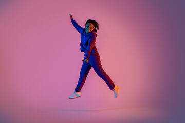 Full length portrait of excited black woman in sportswear jumping on pink neon background, free space