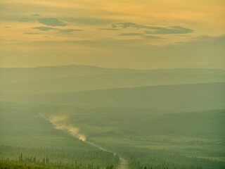 Sunlight and the landscape obscured by the smoke from nearby forest fires as a truck headed for Prudhoe Bay makes it's way up the Dalton Highway outside of Stevens Village Alaska near the Yukon River