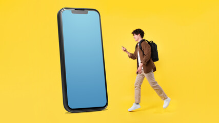 Young Man Walking To Large Smartphone Using Phone, Yellow Background