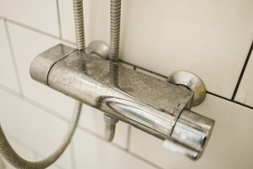 Close-up of shower mixer faucet with limescale, white chalky deposit and stains. Formed on the...