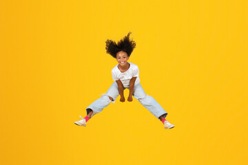 Fototapeta na wymiar Glad excited curly teen african american girl jumping, freezes in air, has fun on empty space