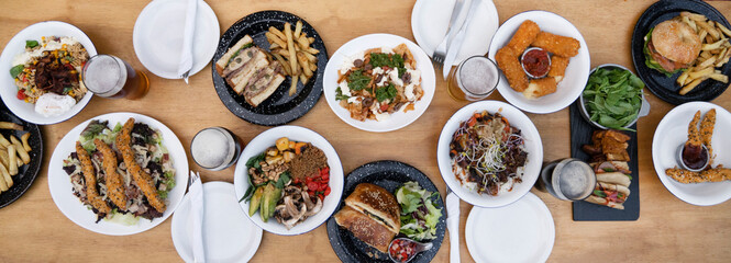 Food banner. Top view of variety of gourmet dishes, tableware and glasses of beer, on the wooden table.