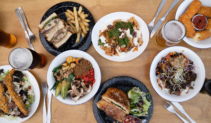 Food. Eating at the restaurant. Top view of variety of gourmet dishes, tableware and glasses of beer, on the wooden table.