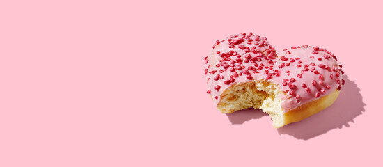 Bitten heart shaped donut with glaze on pink pastel background
