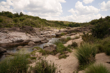 Panorama view of the river flowing across the rocky hill and forest.