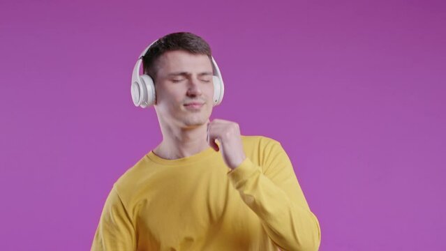 Enjoying young man listening music, slowly dancing with headphones on pink