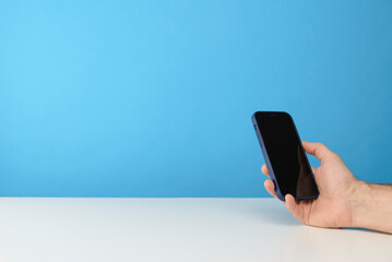 main d'un homme qui tient un smartphone sur fond bleu de studio pour publicité