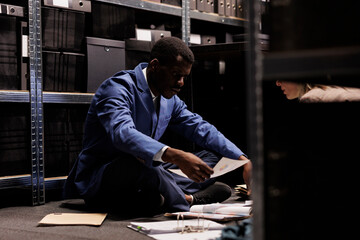 Diverse team sitting on floor in arhive room, working overtime at criminal investigation. Private...