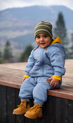 Portrait of a happy cute baby boy sitting outdoor in blue overall and safety boots