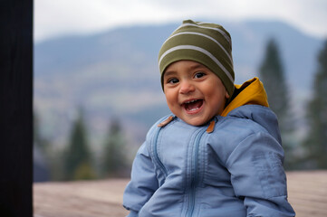 Cheerful cute baby boy laughing while sitting outdoor - happy adorable toddler smiling outdoors