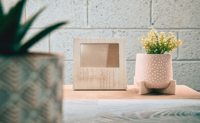 Concept shot of blank wooden photo frame on wooden table with house plant in the pot with brick wall background 