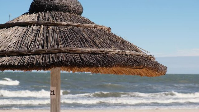 Close up of Straw beach rattan parasol at the empty beach with blue sky backgrounds sea ocean coast. Relaxing day. Idyllic travel and summer vacation concept. Straw umbrella on beautiful tropical