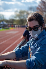 Young man with face mask stands by athletic track vertical image