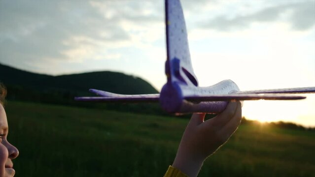 Close up of happy pretty little girl playing with toy airplane on background sky during sunset. Childhood dreams. Family, freedom and airplane concept. Playful cute preteen child pilot. Slow motion