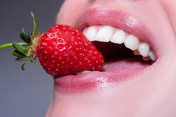 Summer sexy fruits. Closeup of smile with white healthy teeth. Strawberry in lips. Red strawberry in woman mouths close up.
