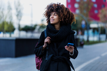 young African American business woman using mobile phone in city of Latin America, Hispanic financial and caribbean people with skyscraper background on winter