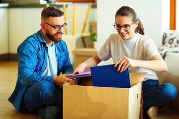 Happy couple looking at photo album while unpacking stuff after relocation to new flat