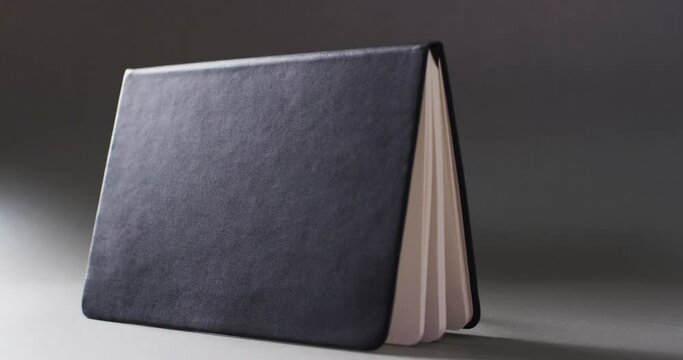 Close up of open black book standing horizontal with copy space on gray background in slow motion
