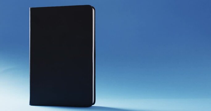 Close up of closed black book standing vertical with copy space on blue background in slow motion