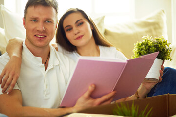 Happy couple looking at photo album while unpacking stuff after relocation to new flat