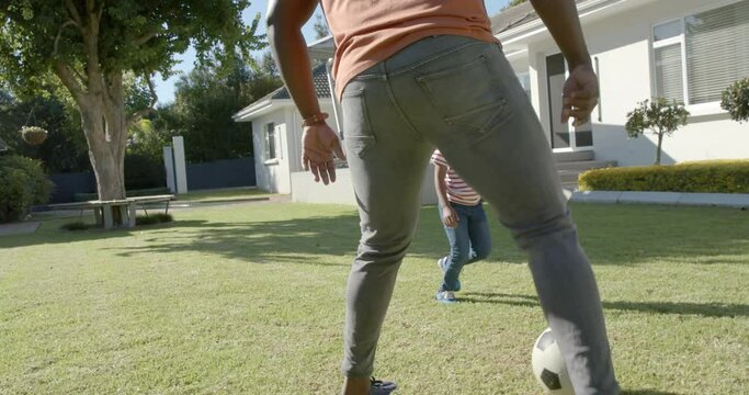 Happy african american father and son playing football in sunny garden, in slow motion
