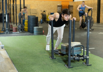Positive fit young European male in sportswear pushing heavyweight plates on prowler slider in...