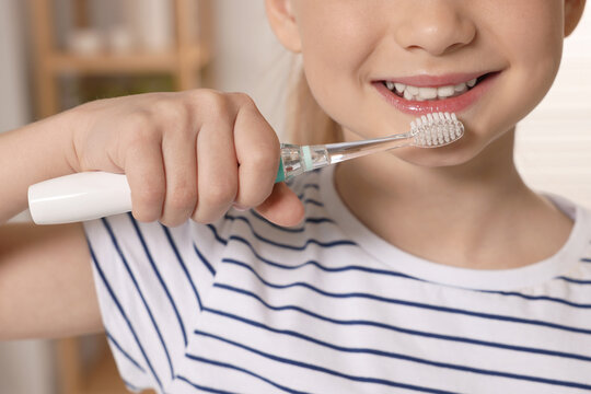 Little girl brushing her teeth with electric toothbrush in bathroom, closeup