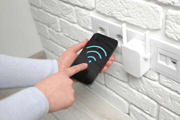 Woman with smartphone connecting to internet via wireless repeater indoors, closeup. Wi-Fi symbol...