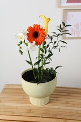 Stylish ikebana as house decor. Beautiful fresh flowers and branch on wooden table near white wall