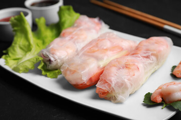 Delicious spring rolls with shrimps wrapped in rice paper served on black table, closeup