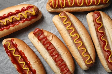Fresh delicious hot dogs with sauces on parchment paper, flat lay