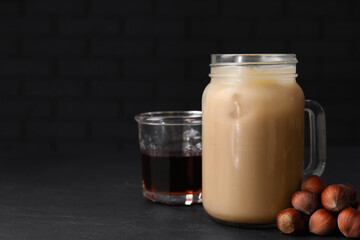 Mason jar of delicious iced coffee, syrup and hazelnuts on black table. Space for text