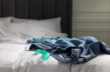 Unrolled condom and jeans on bed in bedroom. Safe sex
