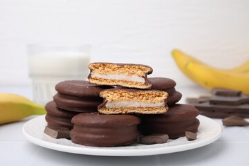 Tasty banana choco pies and pieces of chocolate on white table, closeup