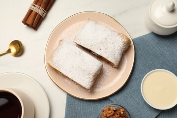 Delicious strudel with powdered sugar served on white marble table, flat lay