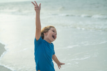 Fototapeta na wymiar Excited child with raised hand run on sea summer beach. Expressive emotional face. Excited little kid running on the beach, walking on sea sandy beach. Summer vacation concept. Lovely kid play outdoor