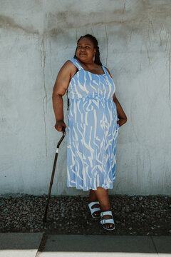 full body afro latinx haitian american woman stands against wall holding black cane