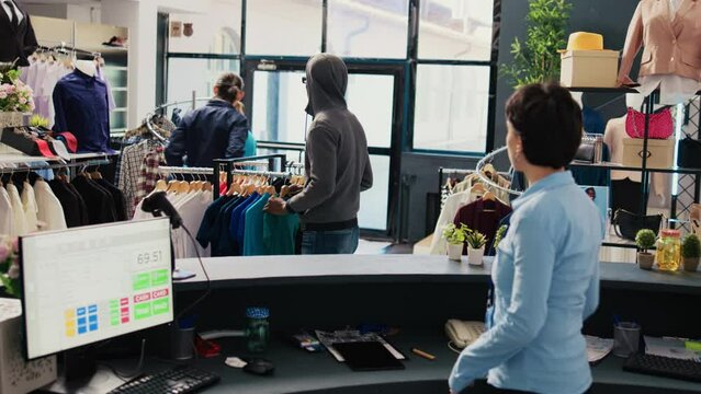 African american robber trying stole stylish shirt being caught by store security guard in shopping mall. Asian bodyguard asking thief to return fashionable merchandise or will call the police