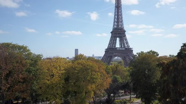 Aerial cinematic drone Paris France Eiffel Tower garden green famous historic landmark from a distance mid day late summer romantic blue sky surrounded by buildings slowly upward motion