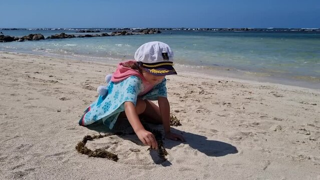little girl with captain hat playing with white sand on a beach. Creativity, holidays, childhood. High quality FullHD footage