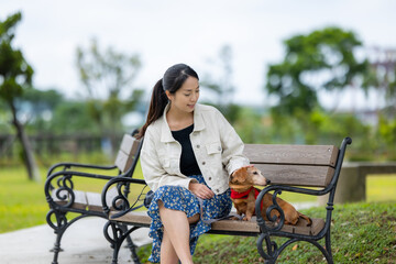 Woman go to the park and sit on the bench with her dachshund dog