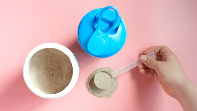 Shaker and scoop with chocolate protein on pink background, top view.