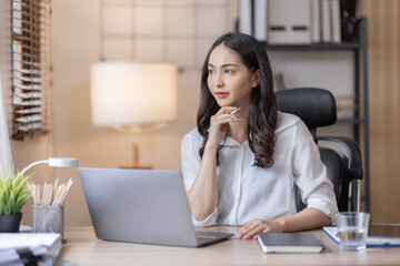 Fototapeta na wymiar Business And Education Concept. Smiling young asian woman sitting at desk working on laptop writing letter in paper documents, free copy space. Happy millennial female studying using laptop