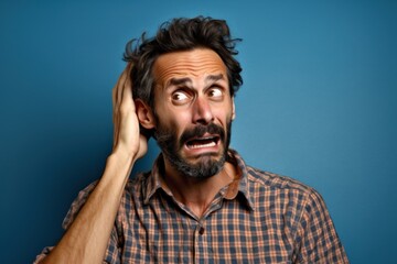 Obraz premium A frustrated man wearing casual attire, expressing exasperation by facepalming against a clean, solid-colored blue background. Frustration and scared facial expression. Generative AI illustration.