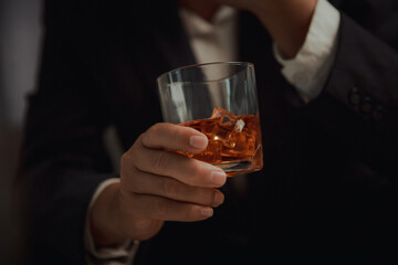 Businessman in black suit holding glass of whiskey Celebrate company success close-up