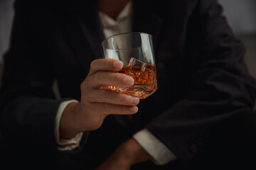 Businessman in black suit holding glass of whiskey Celebrate company success close-up