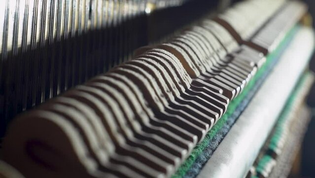 A slow-motion close-up shot of the inside of an old upright piano, showing the hammers and felts striking the strings as someone plays a tune.