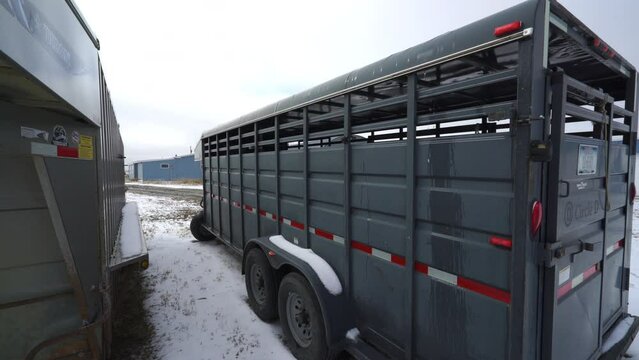 Pan between two large stock trailers with snow melting on spring day